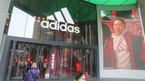 08db5060-3af3-11f0-9a86-f7906cd4e14e 08db5060-3af3-11f0-9a86-f7906cd4e14e Getty Images Adidas shopfront. People are walking through the front doors of a big glass shopfront with the adidas logo above it. The logo is three left-facing rectangles at 45 degrees increasing in size from left to right. On the right of the shop is a massive banner of a model happily wearing an Adidas hooded top. She is smiling broadly. Adidas says customer data stolen in cyber attack 08db5060 3af3 11f0 9a86 f7906cd4e14e