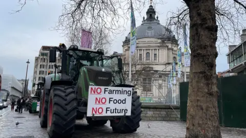 2f0ea830-3180-11f0-9705-29fcd10d0f7c 2f0ea830-3180-11f0-9705-29fcd10d0f7c Malcolm Prior/BBC A green tractor is parked on a Westminster pavement under a grey winter sky next to a bare tree and in front of the QEII Centre. On the front of the tractor is a protest placard that reads No Farming, No Food, No Future. Pedestrians pass by. MPs call for year-long delay to farm inheritance tax MPs call for year-long delay to farm inheritance tax 2f0ea830 3180 11f0 9705 29fcd10d0f7c