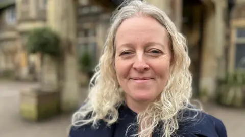 54ac56e0-2cc7-11f0-b295-0f30e97c5fde 54ac56e0-2cc7-11f0-b295-0f30e97c5fde Julie has long, curly blonde hair and is smiling at the camera. In the background is the venue where the Everywoman festival is held. My bowel had to be removed after years of constipation 54ac56e0 2cc7 11f0 b295 0f30e97c5fde