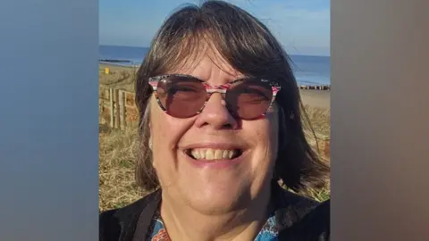 5c701e00-3723-11f0-96c3-cf669419a2b0 5c701e00-3723-11f0-96c3-cf669419a2b0 Julie Brociek-Coulton Julie Brociek-Coulton smiling and looking into the camera. She has short dark hair, and is wearing round tinted glasses with pink, black, and white patterned frames. In the background, there is grass and the sea. Food bank turning people away due to funding gap 5c701e00 3723 11f0 96c3 cf669419a2b0