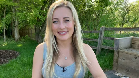 6b26bd40-2a95-11f0-a09e-c5bdc3540c45 6b26bd40-2a95-11f0-a09e-c5bdc3540c45 BBC Eve Morgan, blonde and smiling at the cameras earring a grey vest and small pendant necklace. She is sitting in a garden area with grass and trees behind her Big baby trial gives pregnant women more choice 6b26bd40 2a95 11f0 a09e c5bdc3540c45