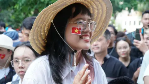 8073bc80-2508-11f0-a735-e704dc71a9bf 8073bc80-2508-11f0-a735-e704dc71a9bf BBC/ Lulu Luo Tung Linh smiles in a hat and with the red and yellow Vietnamese on her cheek. Behind her people are wlaking on the street fifty years after the war, vietnam faces a new us threat - tariffs Fifty years after the war, Vietnam faces a new US threat – tariffs 8073bc80 2508 11f0 a735 e704dc71a9bf