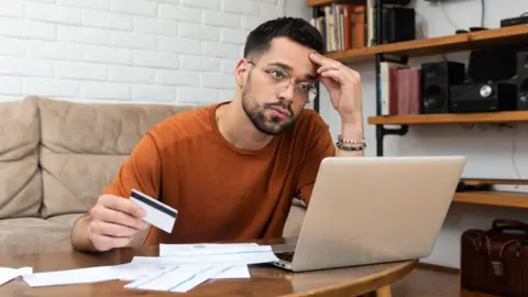 c279a9e0-30c1-11f0-9228-d36f84fd1370 c279a9e0-30c1-11f0-9228-d36f84fd1370 Getty Images Anxious-looking man sits behind a table in a living room, with a laptop, bills and a payment card in front of him. One in 10 have no savings, financial regulator says One in 10 have no savings, financial regulator says c279a9e0 30c1 11f0 9228 d36f84fd1370
