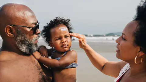 149bed40-4c16-11f0-92ed-e1eefb55eb50 149bed40-4c16-11f0-92ed-e1eefb55eb50 Getty Images On a beach, a mum applies sunscreen to her young daughter who is in her father's arms. What does hot weather do to the body? 149bed40 4c16 11f0 92ed e1eefb55eb50