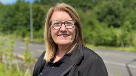 220a7320-5373-11f0-9fdf-1397077316aa 220a7320-5373-11f0-9fdf-1397077316aa Karen Jones, who runs GoodLives charity in Cumbria, is pictured smiling. She has brown hair with blonde highlights and is wearing glasses which have dark frames. She is wearing a black work uniform which displays the charity's logo. Plans to help benefits recipients into work 'a mess', say DWP officials 220a7320 5373 11f0 9fdf 1397077316aa