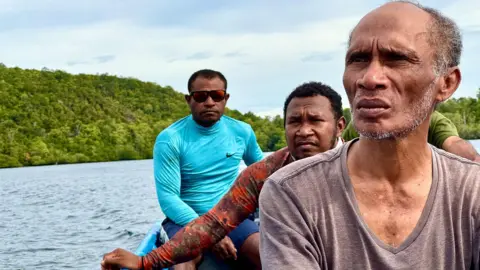 497fdd40-4852-11f0-8a8e-21cdcf60d74e 497fdd40-4852-11f0-8a8e-21cdcf60d74e Global Witness Three men, all environmental activists in Indonesia, sit in a small boat and explore the islands in Indonesia's Raja Ampat. Lush forests of the small islands can be seen in the background. Race to mine metals for EV batteries threatens marine paradise 497fdd40 4852 11f0 8a8e 21cdcf60d74e