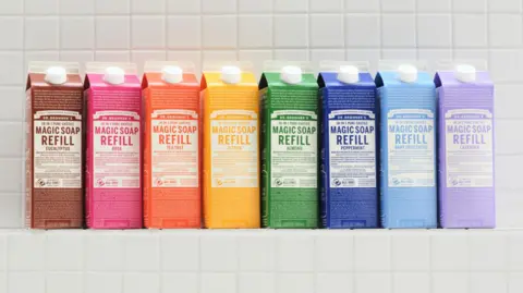 6b651f90-5015-11f0-8c0a-5b816c079050 6b651f90-5015-11f0-8c0a-5b816c079050 Dr Bronner's A row of eight refill packs of Dr Bronner's Magic Soap in many bright colours lined up on a white-tiled shelf. The global environmental award hit by accusations of greenwashing 6b651f90 5015 11f0 8c0a 5b816c079050