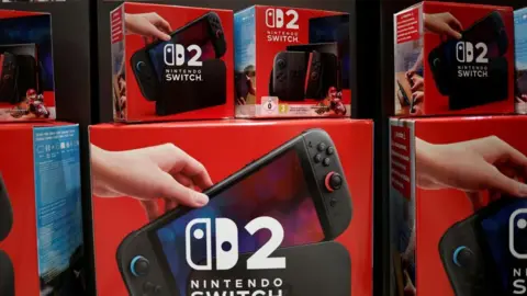 7119fce0-50fa-11f0-a466-d54f65b60deb 7119fce0-50fa-11f0-a466-d54f65b60deb Reuters Red boxes of Nintendo Switch 2 consoles are piled up in a shop window. The box shows the console itself with along with the Nintendo Switch logo. 'New video games cost me a whole day's wages' 7119fce0 50fa 11f0 a466 d54f65b60deb