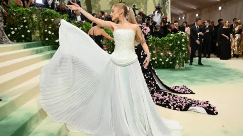 80e627a0-3f86-11f0-bd50-3fddfb5eed43 80e627a0-3f86-11f0-bd50-3fddfb5eed43 Getty Images Singer Ariana Grande is on the red carpet at the Met Gala 2024 in New York. She is wearing a floor-length, white ballgown and is showing off the pleats on the bottom. She has her head turned to the side and her long, blonde hair is tied back in a ponytail. Jonathan Anderson makes history as Dior's new creative director 80e627a0 3f86 11f0 bd50 3fddfb5eed43