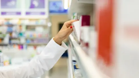 8a943370-3f2a-11f0-90bf-4733dc6be4e0 8a943370-3f2a-11f0-90bf-4733dc6be4e0 Getty Images Woman takes a box of medicine from a shelf lined with boxes of medicine. She has red nail varnish on her nails. Pharmacists warn drug shortage affecting cancer patients 8a943370 3f2a 11f0 90bf 4733dc6be4e0