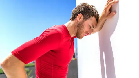 a3996890-4b8c-11f0-8efc-193ffd471116 a3996890-4b8c-11f0-8efc-193ffd471116 Getty Images A sweating man with brown hair and wearing a red top leans against a white wall in the sun because he is overheating. What to do if you think someone has heat exhaustion or heatstroke a3996890 4b8c 11f0 8efc 193ffd471116