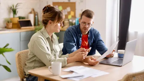 bd52a1a0-476a-11f0-af7d-d7c0845357d2 bd52a1a0-476a-11f0-af7d-d7c0845357d2 Getty Images Man and woman sit at a kitchen table with a laptop, bills and a phone, with a noticeboard behind them. Council tax expected to rise by 5% a year bd52a1a0 476a 11f0 af7d d7c0845357d2