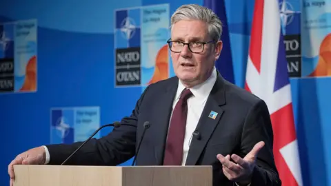 bd629810-535b-11f0-b4be-8f7caf53b80c bd629810-535b-11f0-b4be-8f7caf53b80c PA Media Keir Starmer gestures with his hand while speaking at a Nato summit on Wednesday in the Hague, he's wearing a suit and tie and glasses and stands at a podium with the UK flag in the background against a blue wall with the Nato logo on. Starmer U-turns on benefits cuts after Labour backlash bd629810 535b 11f0 b4be 8f7caf53b80c