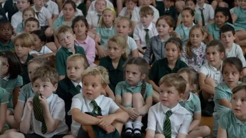 fd6d6c90-533e-11f0-8ce0-e163ca65b455 fd6d6c90-533e-11f0-8ce0-e163ca65b455 BBC Primary school pupils sit and listen, some with quizzical expressions. School sun safety lessons trialled to tackle skin cancer fd6d6c90 533e 11f0 8ce0 e163ca65b455