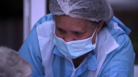151f46b0-536c-11f0-b4be-8f7caf53b80c 151f46b0-536c-11f0-b4be-8f7caf53b80c BBC A care worker in a face mask and other personal protective equipment leans towards a care home resident. This shot was taken in April 2020. Covid inquiry to look at impact on care services 151f46b0 536c 11f0 b4be 8f7caf53b80c