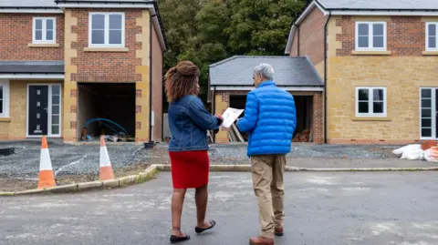 19daa190-5c90-11f0-8547-e5153bdee31d 19daa190-5c90-11f0-8547-e5153bdee31d Getty Images Man and woman outside new build homes Housebuilders to pay £100m to avoid legal decision 19daa190 5c90 11f0 8547 e5153bdee31d