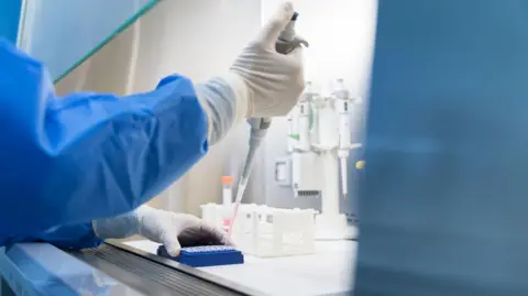 Getty Images Laboratory worker in blue protective clothing and white gloves working with lab equipment and containers on the workbench  New science centre aims to help fight pandemics 24140410 62f0 11f0 9af5 ebd4b3001234