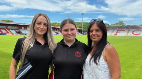 3ce14db0-5592-11f0-a9c4-6559fc28b390 3ce14db0-5592-11f0-a9c4-6559fc28b390 Hannah Marsh, Gracie and Nadina Hill stand on the pitch at Stevenage Football Club with stands in the background Household energy bills fall but may not go much lower 3ce14db0 5592 11f0 a9c4 6559fc28b390