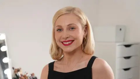 4ec4ed30-5bcc-11f0-b5db-0b5f00d743e4 4ec4ed30-5bcc-11f0-b5db-0b5f00d743e4 BBC Amy, who has shoulder length blonde hair and wears a sleeveless black top, smiles at the camera. Behind her is a mirror and a number of makeup brushes Latin makeup labels put people with allergies 'at risk' 4ec4ed30 5bcc 11f0 b5db 0b5f00d743e4