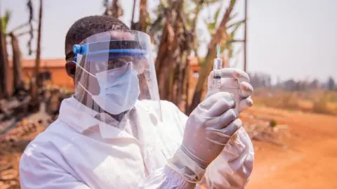 508f6dd0-5e5a-11f0-b6ea-43a0f3805f7e 508f6dd0-5e5a-11f0-b6ea-43a0f3805f7e Getty Images A medic in full protective face mask and white clothing, standing outside, holding up a syringe with gloved hands Vaccine roll-outs cut deaths by 60% – study 508f6dd0 5e5a 11f0 b6ea 43a0f3805f7e