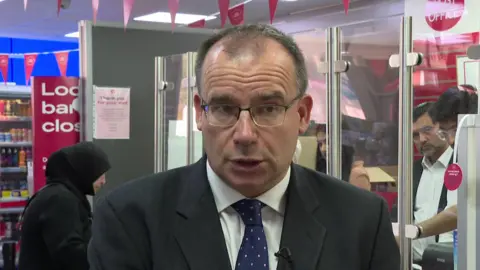 55ad80b0-60b0-11f0-94ee-eb2aebfd2fbb 55ad80b0-60b0-11f0-94ee-eb2aebfd2fbb Post Office Minister Gareth Thomas in suit and tie, standing in front of a Post Office counter, with customer and staff in the background Post Office could be owned by its postmasters, government says 55ad80b0 60b0 11f0 94ee eb2aebfd2fbb