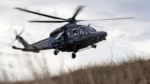 91371f90-6314-11f0-9a60-b70603b839b2 91371f90-6314-11f0-9a60-b70603b839b2 Leonardo Helicopters A helicopter flying. It is black. The camera is looking up. Grass on the floor is blowing from the rotors. Defence firms 'confident' hundreds more jobs will come 91371f90 6314 11f0 9a60 b70603b839b2