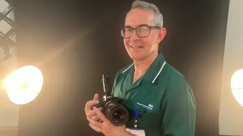 92cd79a0-5674-11f0-95fc-edf89039c20a 92cd79a0-5674-11f0-95fc-edf89039c20a Jason Randall a medical photographer holding a digital camera used to photograph skin lesions. He is pictured in the special studio set up for patients at Nottinghamshire's King's Mill hospital Digital imaging cuts waiting times for skin cancer 92cd79a0 5674 11f0 95fc edf89039c20a