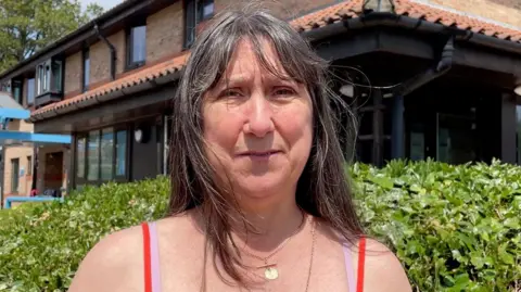 aa7ee070-5813-11f0-81c2-eddd1d437243 aa7ee070-5813-11f0-81c2-eddd1d437243 Kit Taylor/BBC A woman with brown hair looking directly into the camera, with a serious expression. She is wearing a bright orange vest with straps and two golden necklaces. 'Menopause made me forget my name' aa7ee070 5813 11f0 81c2 eddd1d437243