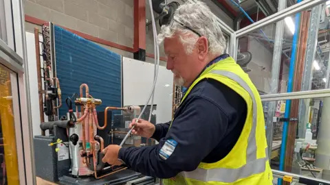 cebb5fa0-5ca9-11f0-960d-e9f1088a89fe cebb5fa0-5ca9-11f0-960d-e9f1088a89fe Chris Baraniuk A man in a hi-viz vest works on a heat pump Heat pump makers are ready for a rush: Will customers come? cebb5fa0 5ca9 11f0 960d e9f1088a89fe